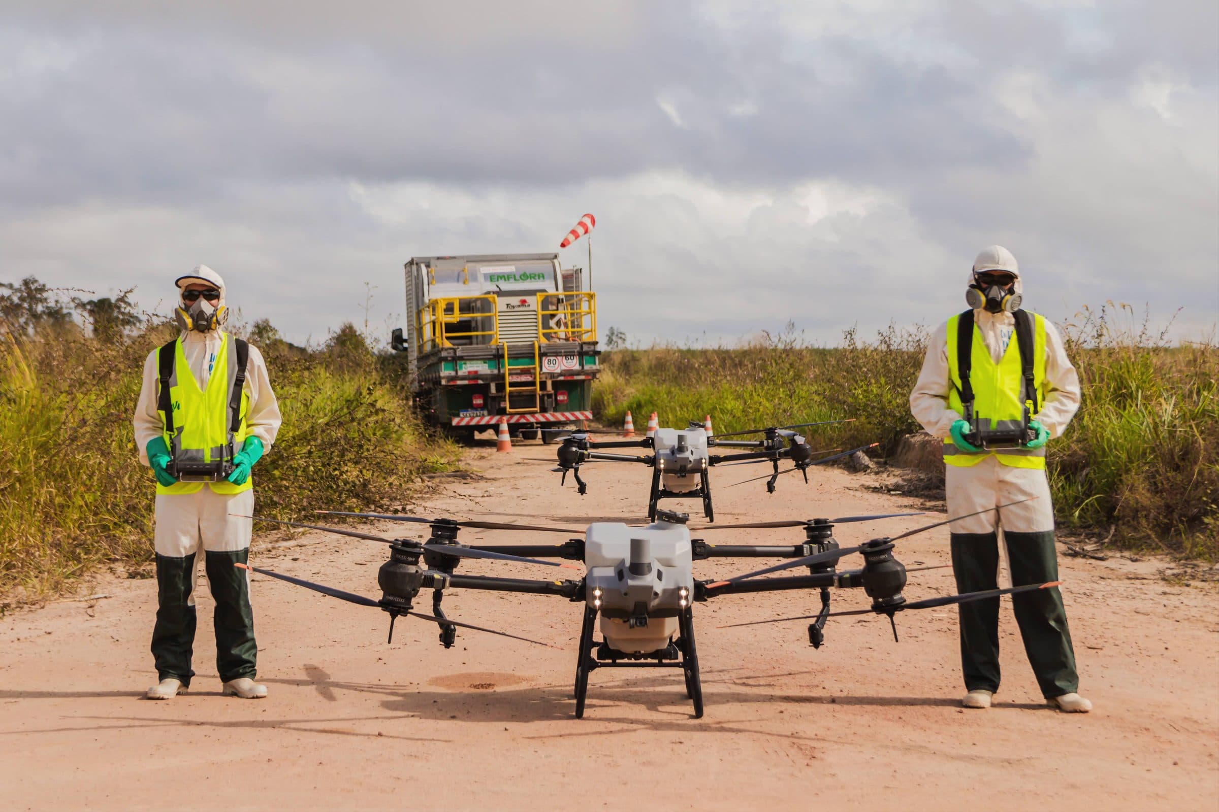 Dos operadores con EPP completo junto a tres drones de pulverización, frente al camión de apoyo de Emflora