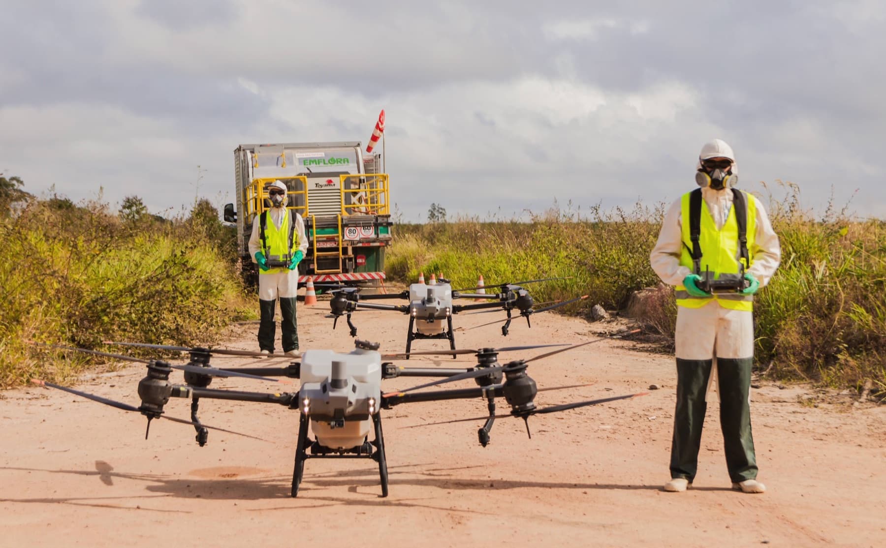 Emflora spray drone in flight, with PPE-equipped operator and support truck